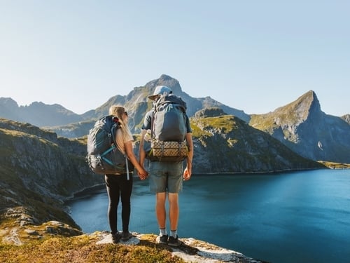 Zwei Personen sind am Gipfel eines Berges angekommen und blicken auf einen großen See.